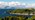 A distant view of Dunollie Wood over the hills behind Oban esplanade with buildings along the shoreline and mountains in the background